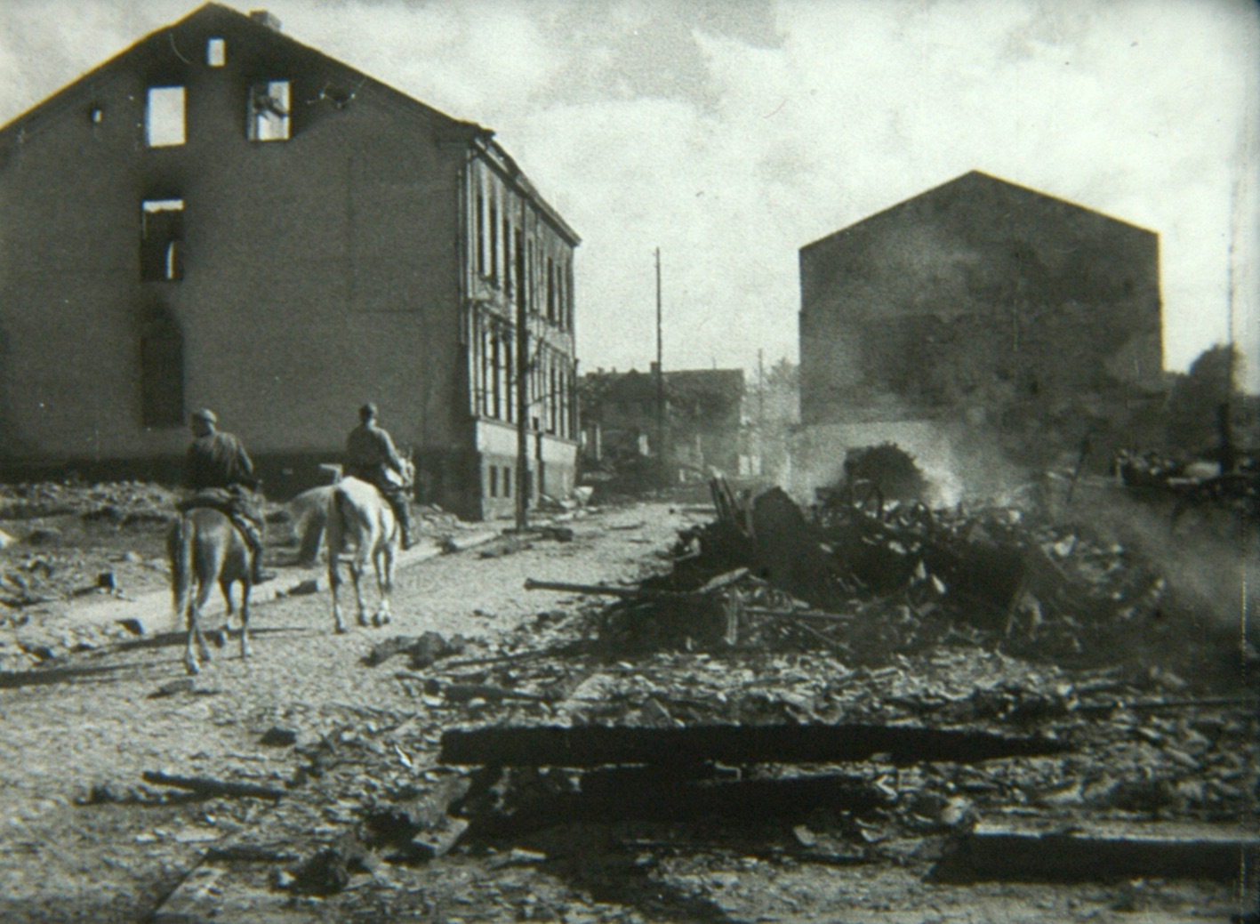 This event poster shows a still of two men on horseback passing by destroyed buildings in the city of Bialystok.