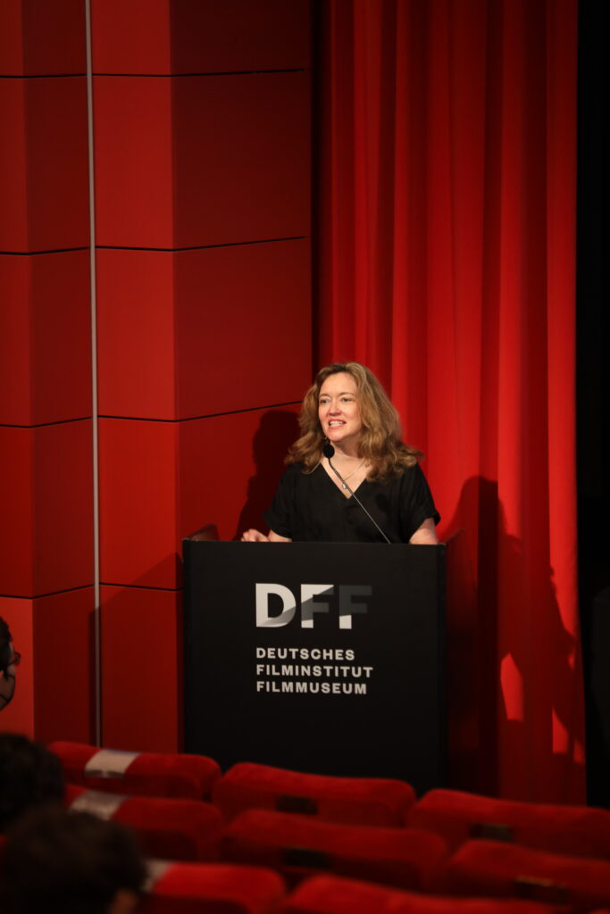 This photo shows a woman welcoming the participants of the conference.