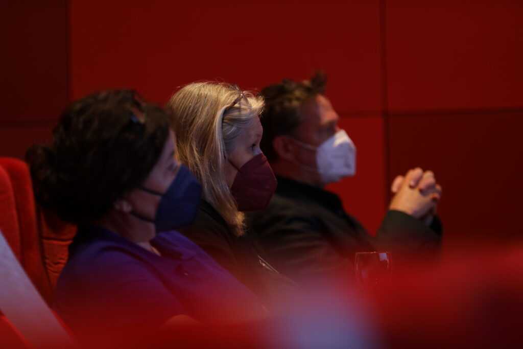 This photo shows two women and a man listening to a lecture in a cinema theatre.