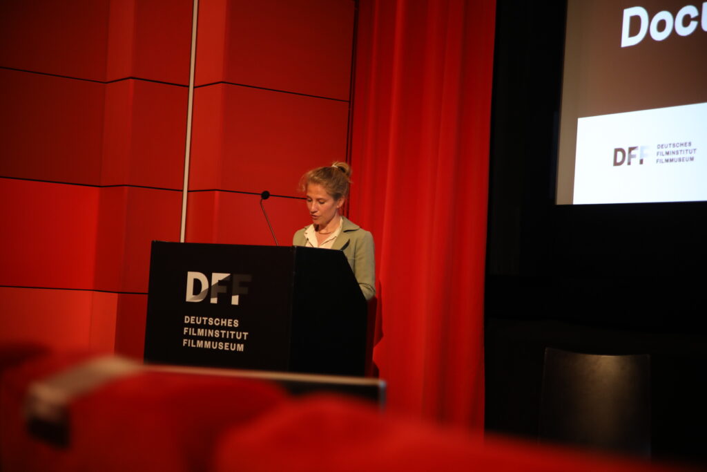 This photo shows a woman introducing speakers at a conference.